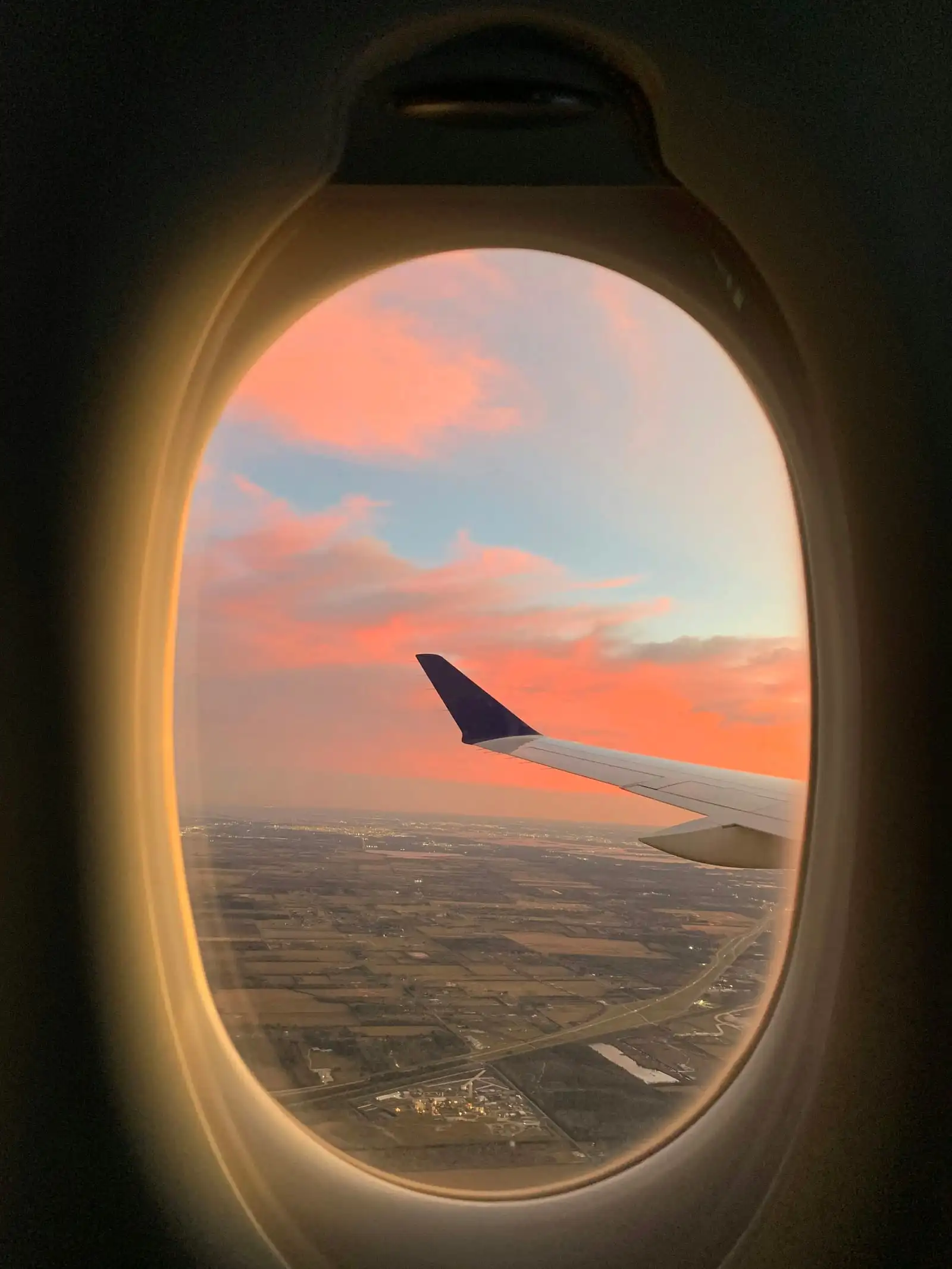 The view from a plane window at sunset: the tip of a wing over flat land far below.
